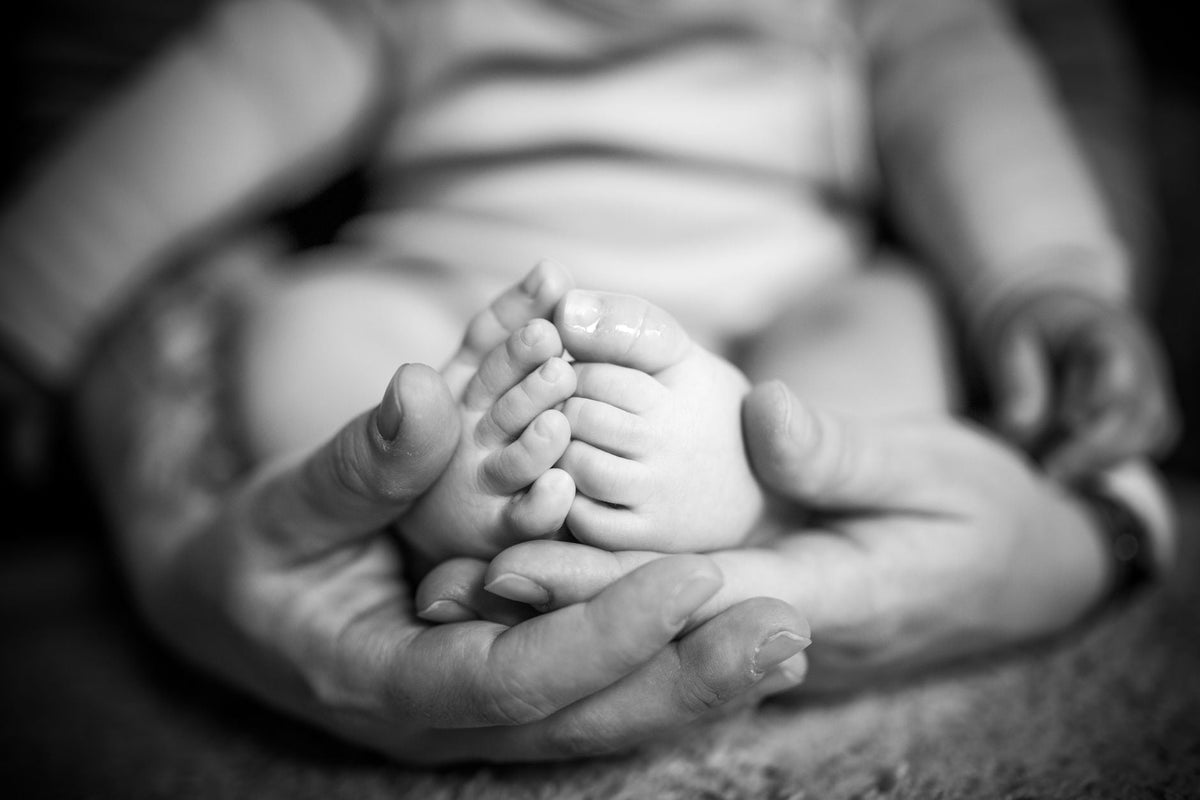Pieds de nouveau-né tenus dans les mains d'un parent - empreinte de bébé | Petit Murmure